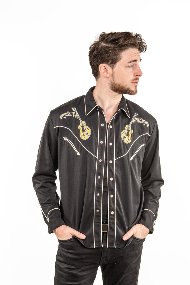 A man wearing a black western-style button-up shirt with gold and white embroidery, posed against a solid white background.