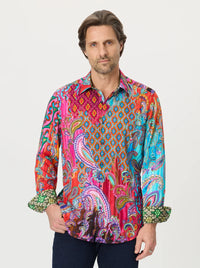 A man wearing a long-sleeve button-up shirt with a vibrant, multicolored paisley and geometric pattern in pink, blue, orange, and green, paired with dark blue jeans, against a light gray background.