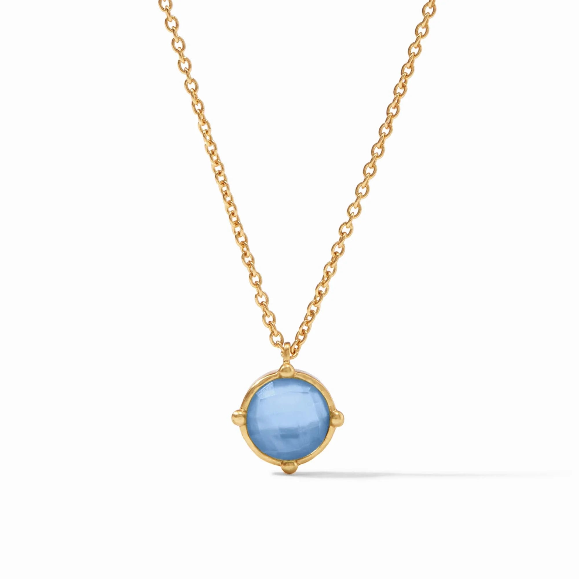 The Honeybee Solitaire Necklace - Iridescent Chalcedony Blue features a 24K gold plate chain and a round, faceted light blue gemstone pendant in a simple gold bezel. This adjustable necklace adds refined elegance to any look.