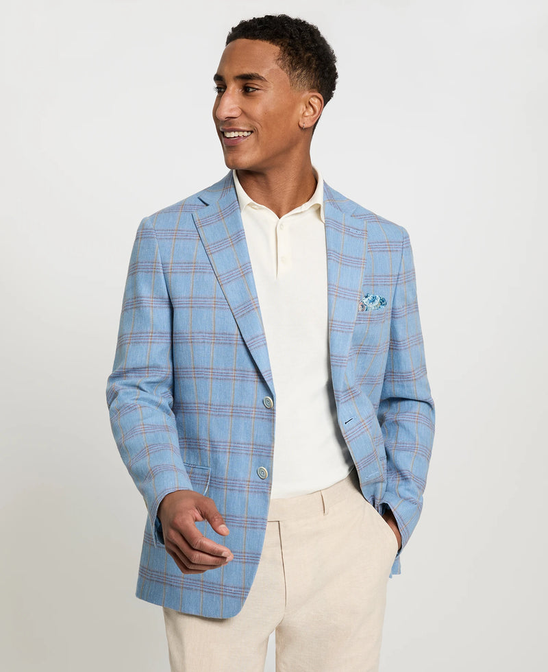 Man wearing a light blue checkered blazer over a white shirt with beige pants on a plain background