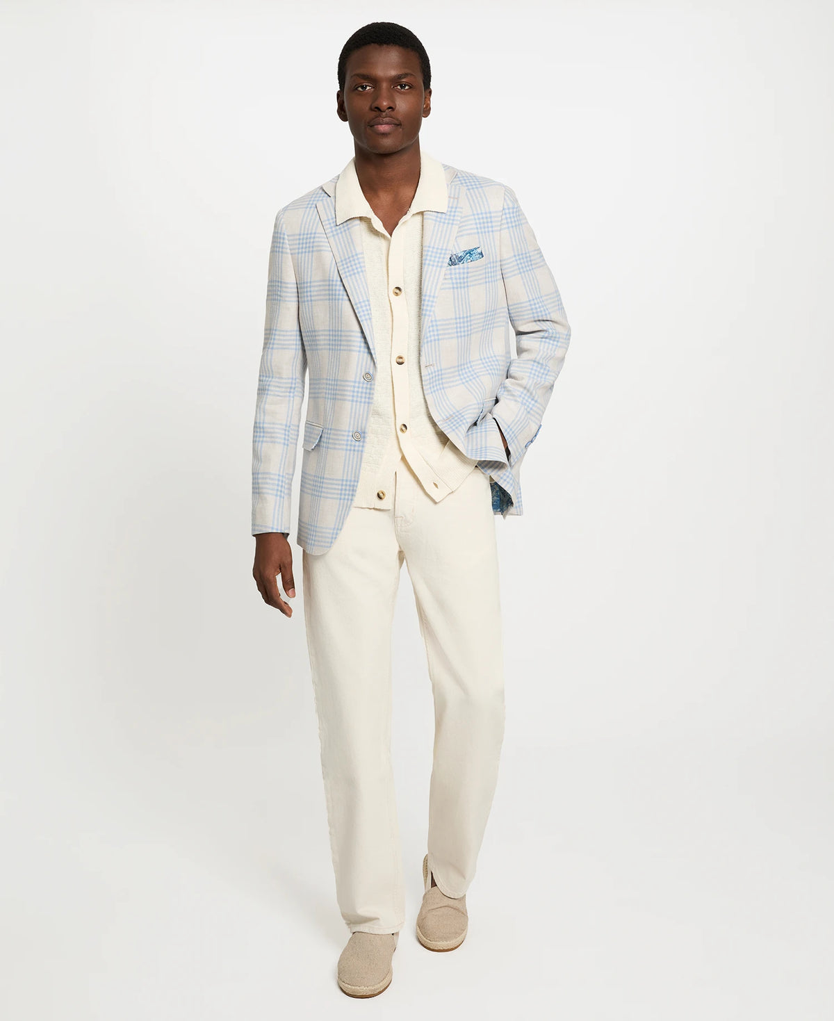 Man wearing a light blue checkered blazer over a white shirt with beige pants on a white background