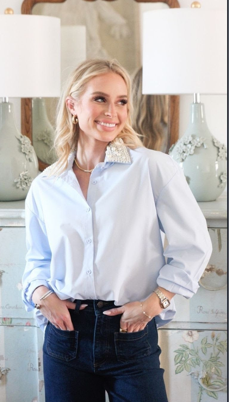A promotional editorial-style photo with the text 'Karlie Palm Beach Edit' at the top and contact details for Haley West at the bottom. The central photo shows a woman wearing a light blue button-up shirt and dark jeans, standing indoors in front of lamps and a console table.